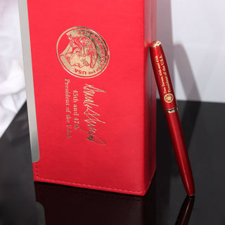 Red executive order pen with gold detailing, placed beside a matching red case featuring presidential insignia.