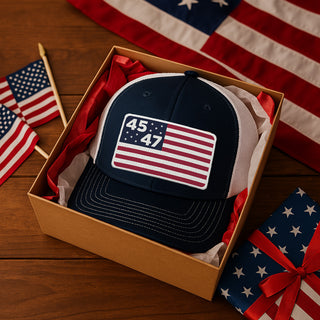 Navy blue trucker hat featuring a flag design with "45" and "47" on a white patch, presented in a gift box.