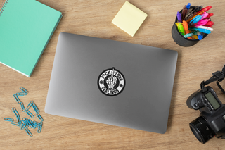 F*ck your feelings decal on a silver laptop, surrounded by stationery items and a camera on a wooden desk.