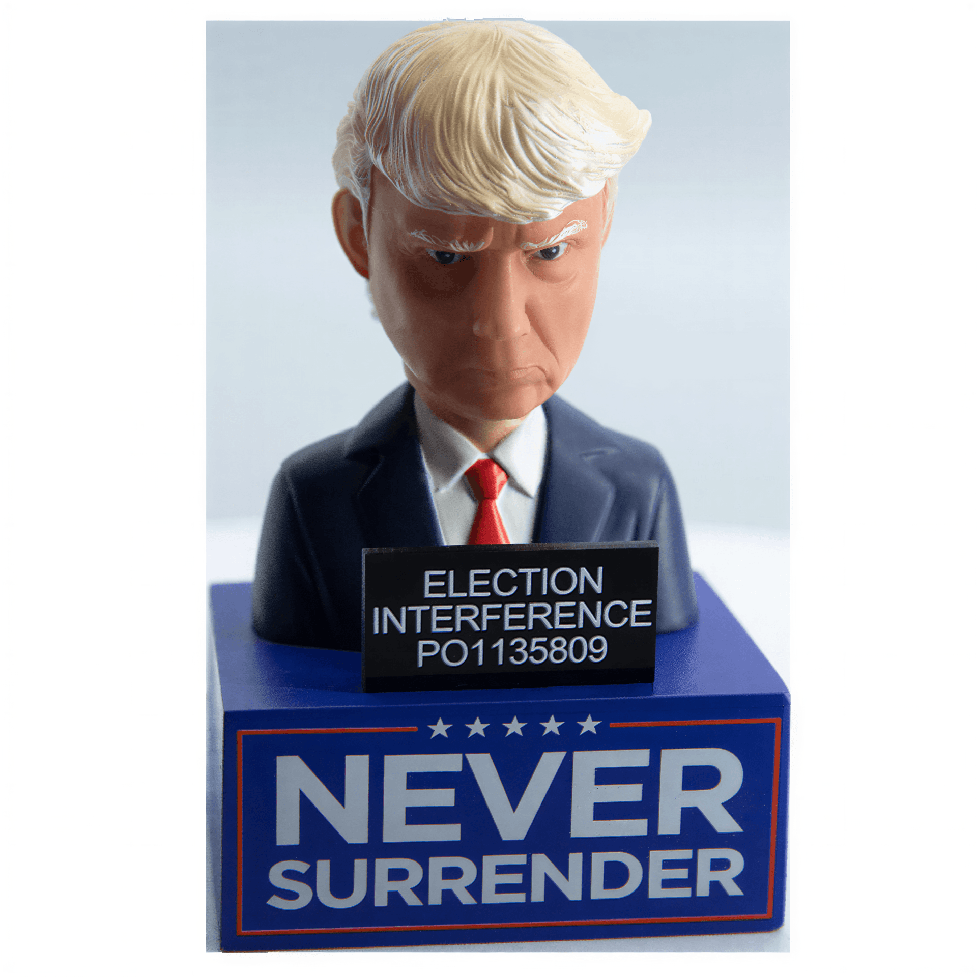 Trump mugshot bobblehead featuring a serious expression, wearing a suit and tie, with a base that reads "Never surrender.